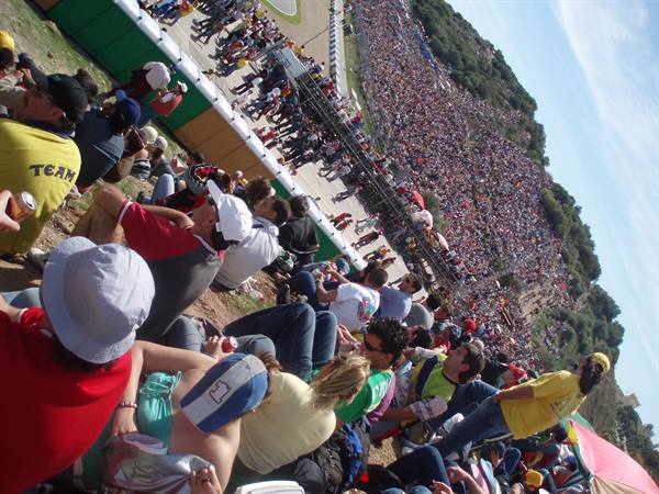 Crowd of spectators sitting on sunny grass beside the race track