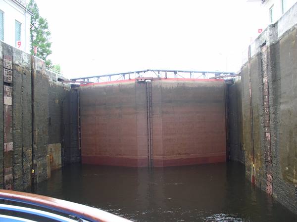 Reddish metal lock gate between tall concrete walls, calm water