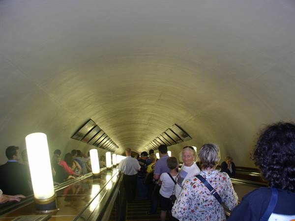 Commuters riding a long escalator inside a metro tunnel with glowing lamps