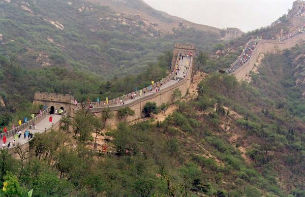 Tourists walk along the stone Great Wall winding over green hills at Badaling