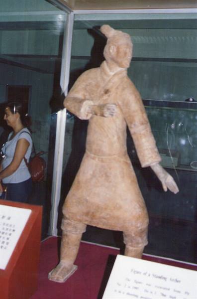 Terracotta warrior statue behind glass, standing archer figure without bow