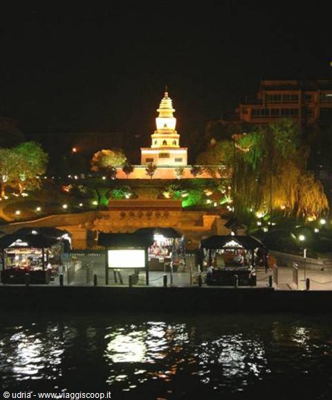 Illuminated pagoda at night reflected on the river among trees and stalls