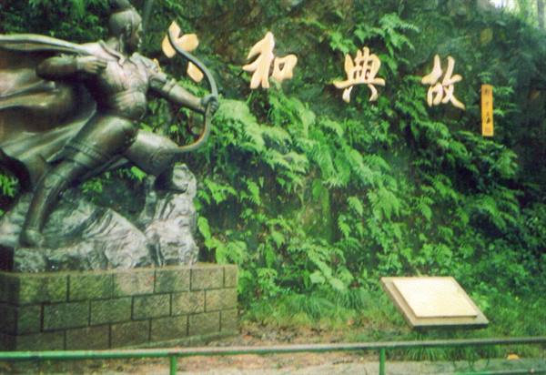 Bronze archer statue at Liuhe Pagoda, golden Chinese characters among green ferns