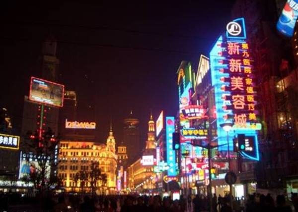 Neon signs glowing at night on Nanjing Road, crowd walking below