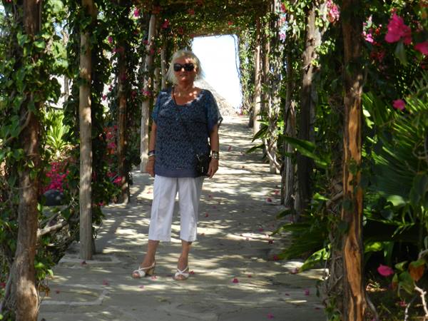 Blonde woman in sunglasses posing under a wooden pergola covered with bougainvillea