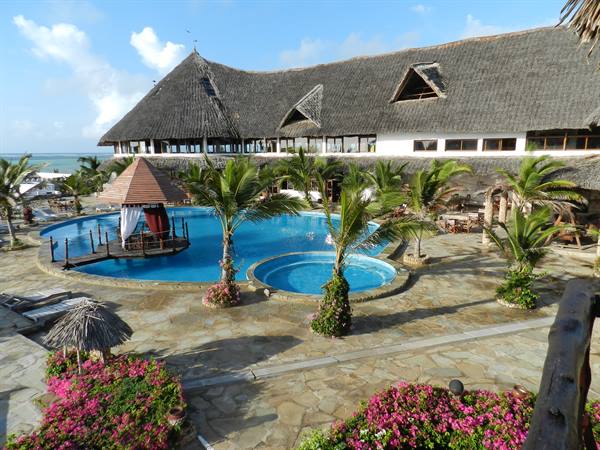 Blue pool with palm trees and thatched roofs at a seaside resort