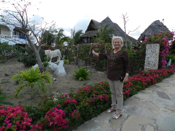 Blonde woman points at a leopard statue in a resort garden with bougainvillea
