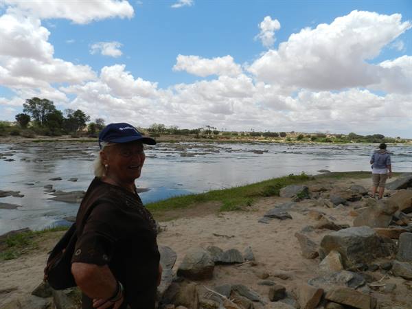 Woman in blue cap on rocky riverbank of wide river, cloudy sky