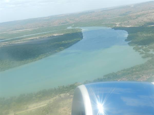 Turquoise river winding through mangroves seen from airplane window, engine glinting below