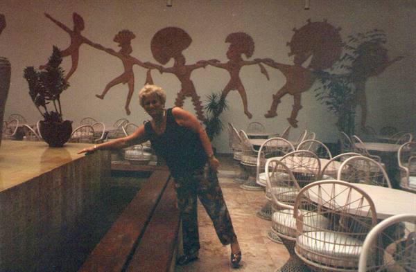 Blonde woman in a restaurant with rattan chairs and dancing metal figures