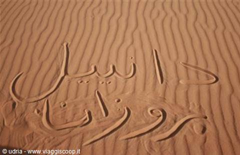 Arabic writing traced in the orange sand of a dune