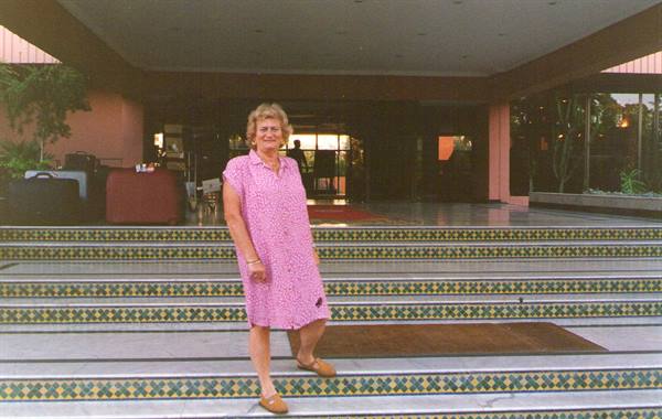 Woman in pink dress poses on mosaic steps in front of a hotel