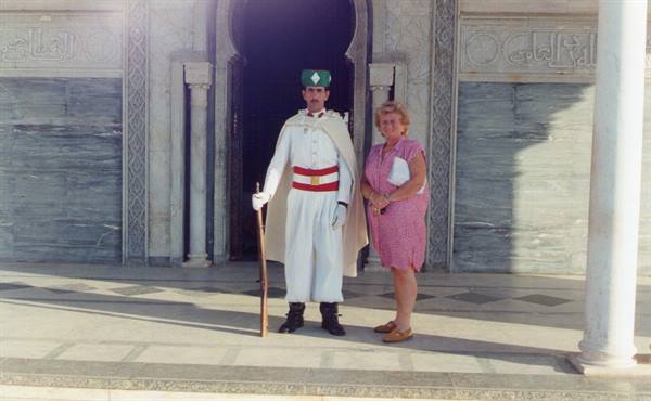 Tourist next to the white-uniformed royal guard at Mohammed V Mausoleum, marble and sunlight