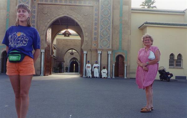 Tourists before the royal palace mosaic gate, guards in white under the arch
