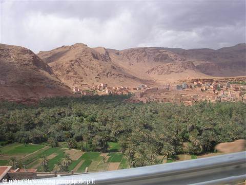 Mud-brick village above a palm grove, arid mountains under cloudy skies