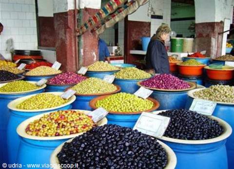 Market stall with blue tubs full of colorful olives, vendor in background