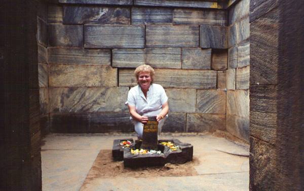 Woman in white crouching at sacred stone with flower offerings inside granite shrine