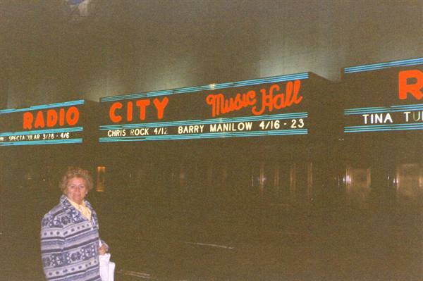 Woman standing in front of the lit Radio City Music Hall marquee at night