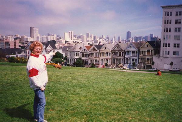 Woman points at the Painted Ladies from Alamo Square, green lawn and San Francisco skyline