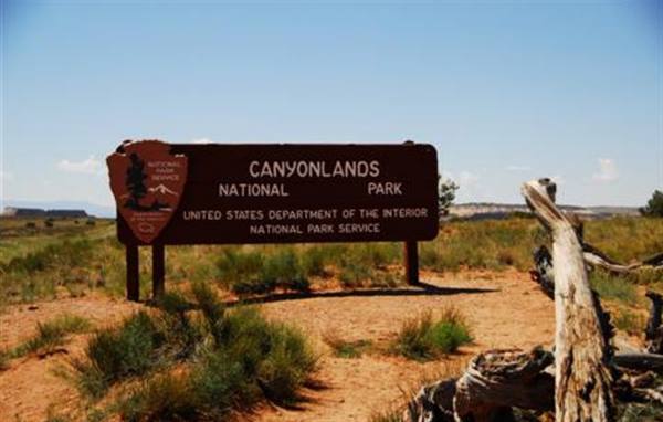 Wooden Canyonlands National Park sign among shrubs and red sand