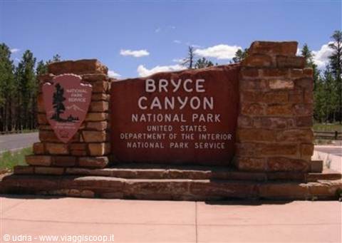 Red stone entrance sign at Bryce Canyon National Park, blue sky and pine trees
