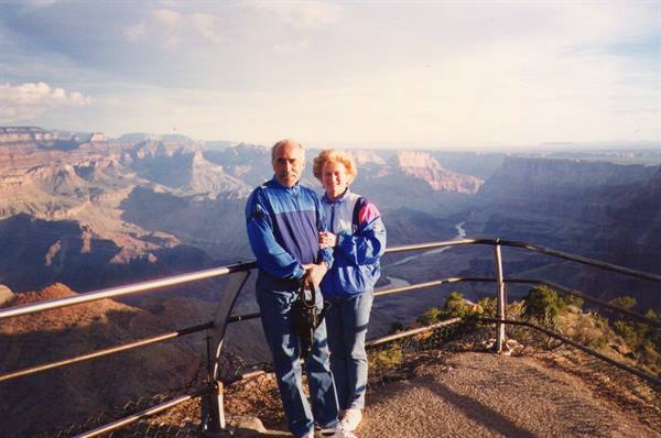 Elderly couple in blue jackets by the metal railing, Grand Canyon and Colorado River behind