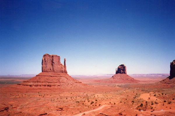 Monument Valley: red sandstone buttes under blue sky, sandy desert