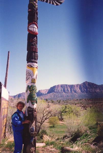 Woman beside a large painted wooden totem pole, rocky mountains behind
