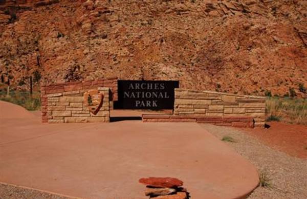 Stone and wood sign at the entrance of Arches National Park among red rocks