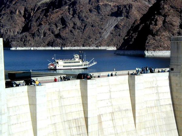 White paddle steamer on Lake Mead, Hoover Dam concrete wall, tourists walking above