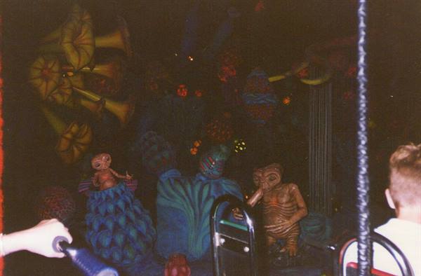Child on dark ride vehicle among glowing alien statues and luminous flowers