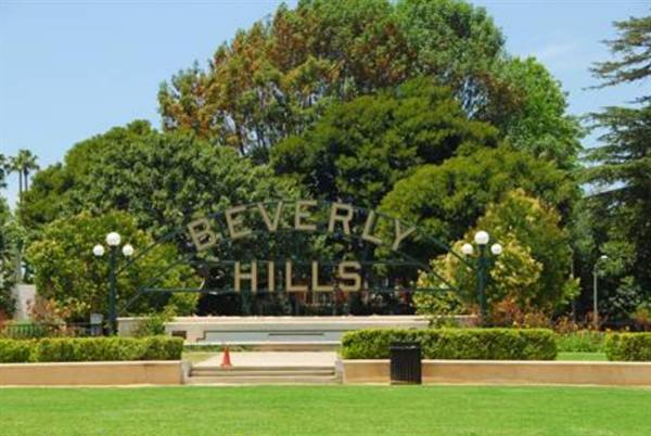Beverly Hills metal sign among green trees and manicured lawn, daylight