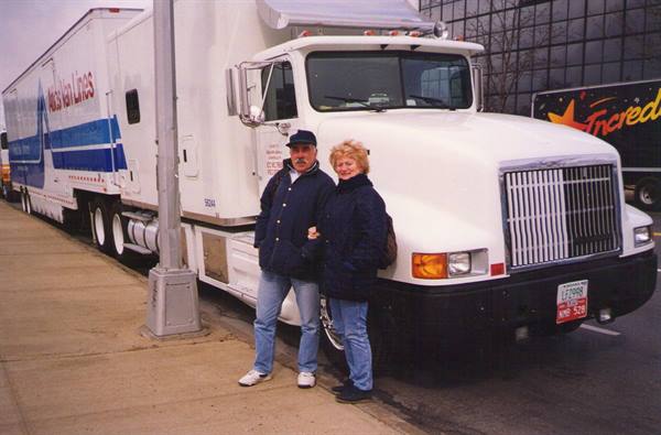 Couple standing beside a white Moore Van Lines truck parked on the street