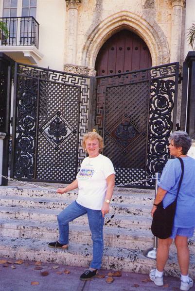 Woman in white t-shirt and jeans on steps before an ornate wrought iron gate