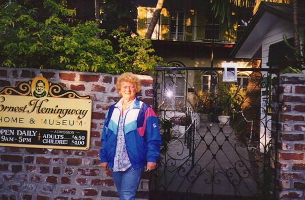 Smiling woman beside the wrought-iron sign of the Ernest Hemingway Home & Museum, Key West