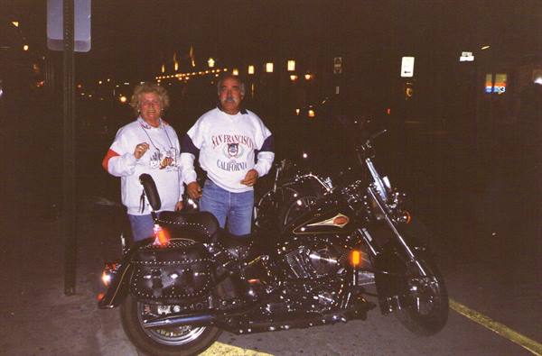 Couple standing beside a black Harley motorcycle at night, San Francisco sweatshirt