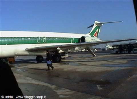 Alitalia jet with green livery and tricolor tail, man walking on wet tarmac