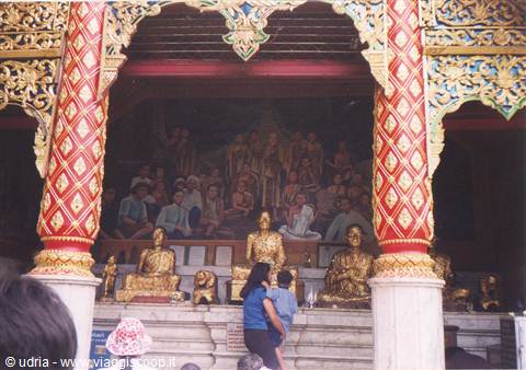 Buddhist temple: red and gold columns, Buddha statues, worshippers before a mural