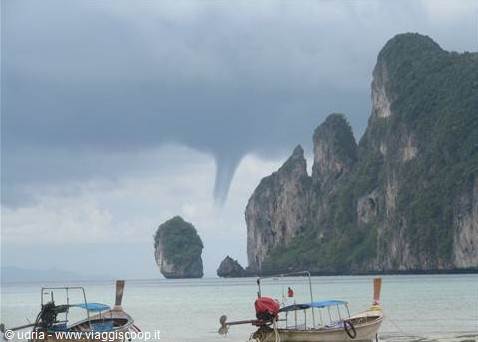 Longtail boats on the beach, limestone cliffs and a waterspout offshore, Thailand
