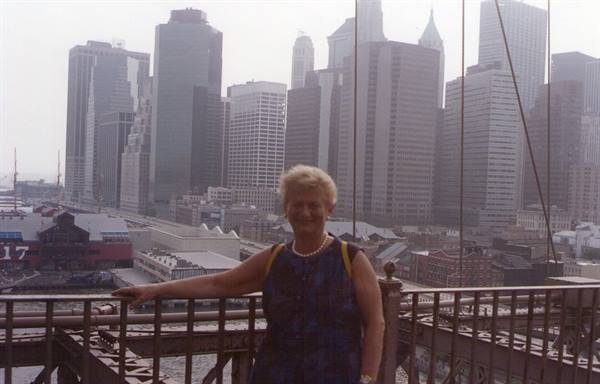 Woman on Brooklyn Bridge railing, Manhattan skyscrapers behind morning haze