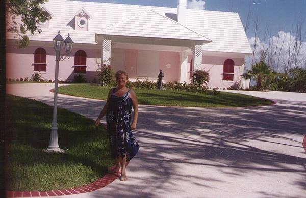 Woman in blue dress walks barefoot in front of pink villa with white roofs