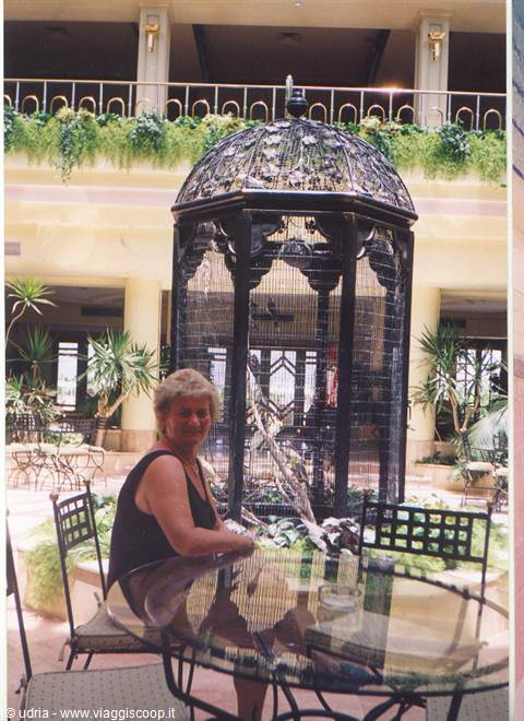 Woman at glass table in front of large wrought iron birdcage in hotel atrium