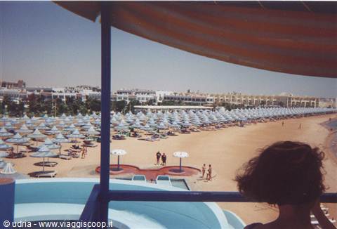 Beach with white sunshades and parasols, red canopy overhead, tourist in silhouette