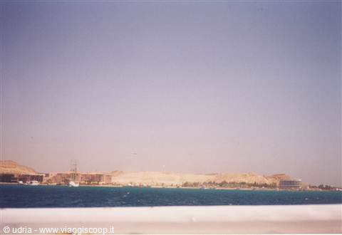 turquoise sea in front of a desert coast with hotels and sandy hills