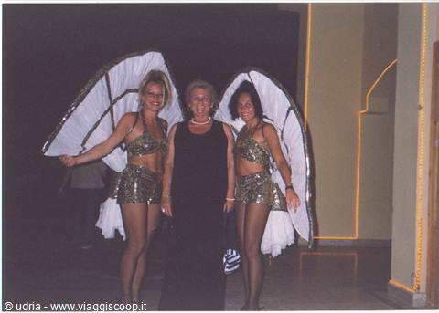 Woman in black with two dancers in sequins and large white wings