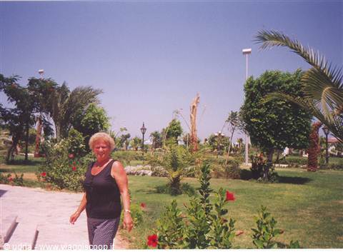 Blonde woman in black tank top walks through gardens with palms and hibiscus