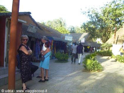 Tourists near thatched-roof market stalls along a sunny village path