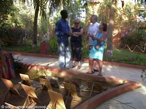 Tourists chat with a painting vendor among easels in a palm garden