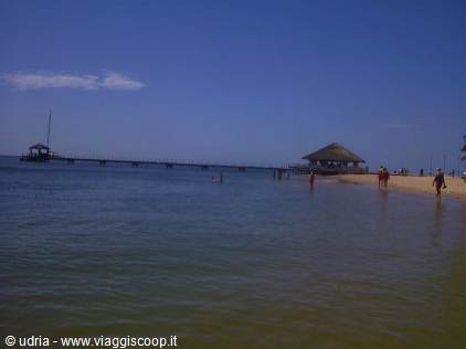 Wooden pier over the sea with thatched hut on the beach, tourists wading in shallow water
