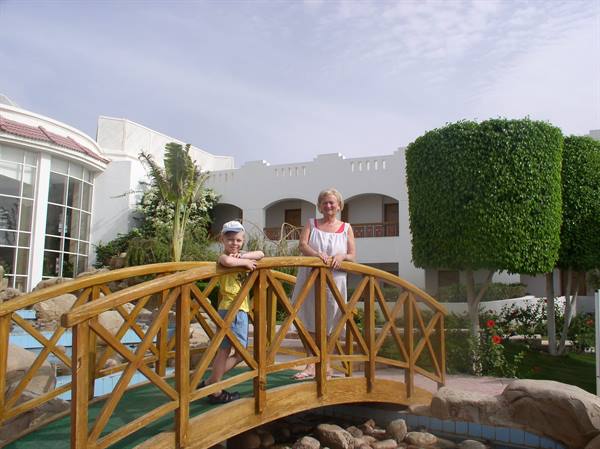 Woman and child on a wooden bridge at a resort with palms and hedges